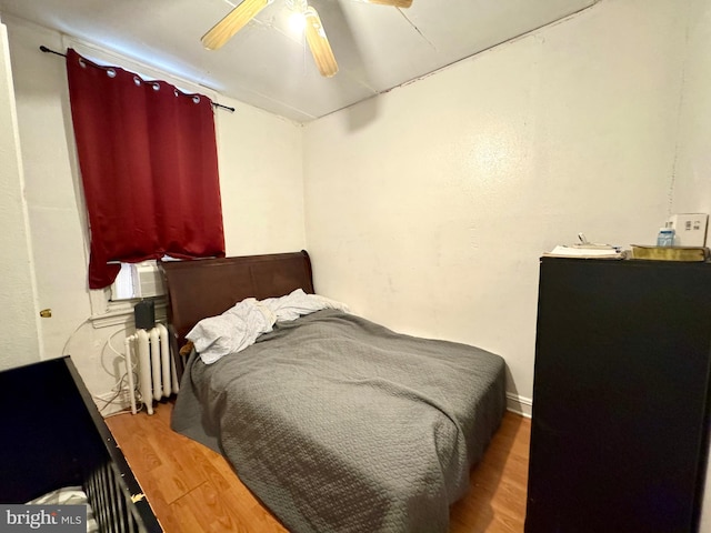 bedroom featuring radiator heating unit, hardwood / wood-style flooring, ceiling fan, and cooling unit