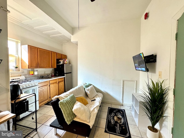 kitchen featuring sink, stainless steel fridge, light tile patterned floors, tasteful backsplash, and white gas stove