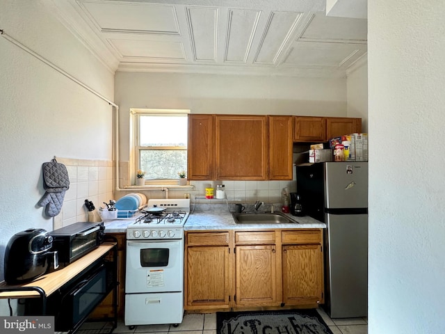 kitchen with sink, decorative backsplash, light tile patterned floors, white gas range, and stainless steel refrigerator