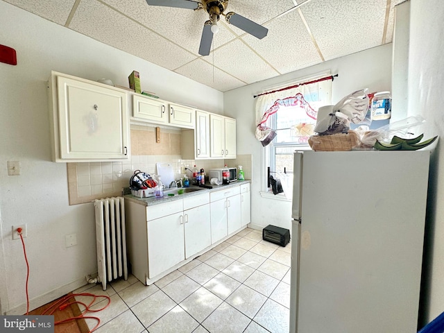 kitchen with a drop ceiling, radiator, white cabinets, white refrigerator, and light tile patterned floors