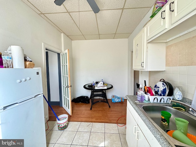 kitchen featuring a drop ceiling, sink, white refrigerator, white cabinets, and light tile patterned flooring