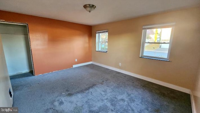 unfurnished bedroom featuring a closet, dark carpet, and multiple windows