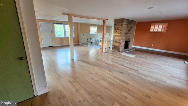 unfurnished living room with light wood-type flooring and a stone fireplace