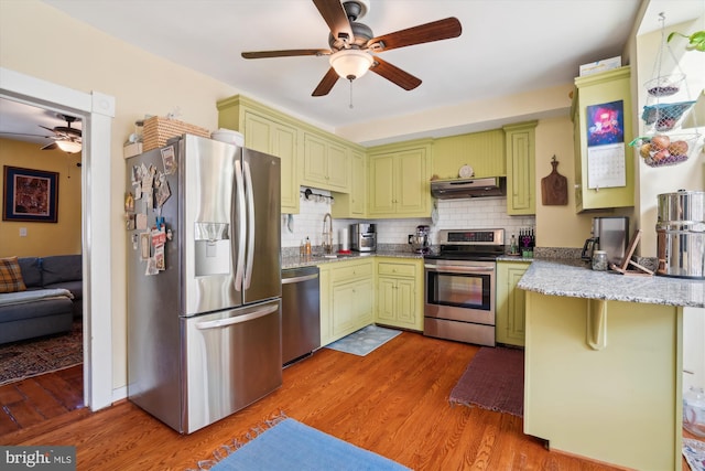 kitchen with tasteful backsplash, wood-type flooring, appliances with stainless steel finishes, exhaust hood, and kitchen peninsula