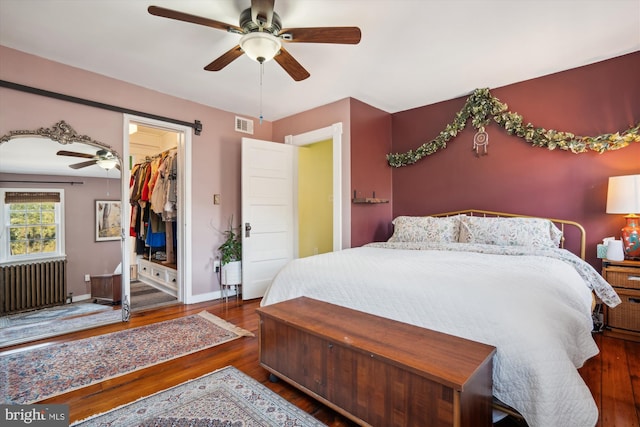 bedroom featuring radiator, ceiling fan, a walk in closet, and dark hardwood / wood-style flooring