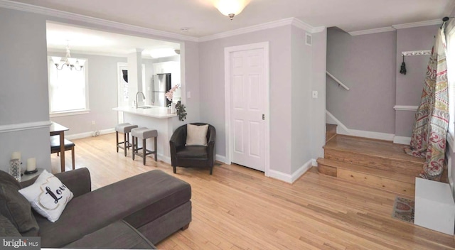 living room featuring ornamental molding, a chandelier, light wood-type flooring, and sink