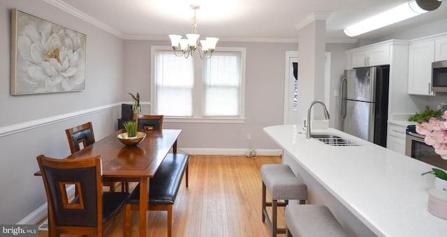 dining room with light hardwood / wood-style flooring, ornamental molding, a chandelier, and sink