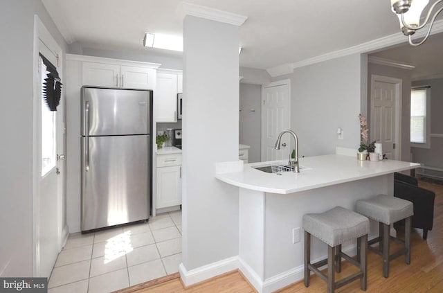 kitchen featuring a breakfast bar area, sink, stainless steel fridge, white cabinets, and light hardwood / wood-style floors