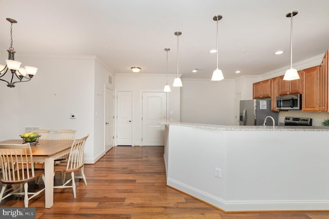 kitchen with hanging light fixtures, hardwood / wood-style flooring, crown molding, and stainless steel appliances