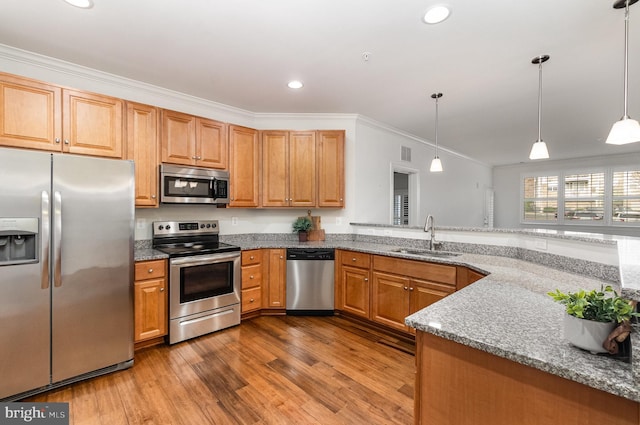 kitchen with light stone counters, light wood-type flooring, appliances with stainless steel finishes, decorative light fixtures, and sink