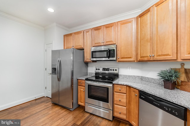 kitchen with ornamental molding, appliances with stainless steel finishes, wood-type flooring, and light stone counters