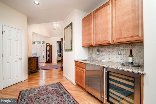 bar with sink, tasteful backsplash, light stone countertops, light wood-type flooring, and wine cooler