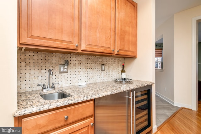 kitchen with beverage cooler, sink, tasteful backsplash, light stone countertops, and light wood-type flooring