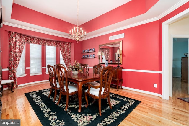 dining area featuring wood-type flooring, a raised ceiling, crown molding, and a notable chandelier