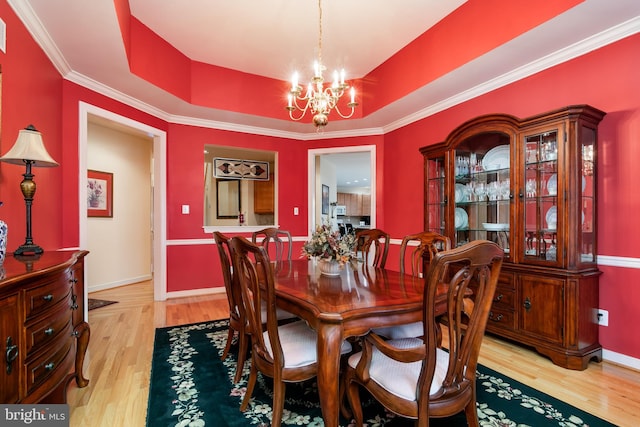 dining room featuring a chandelier, light wood-type flooring, crown molding, and a tray ceiling