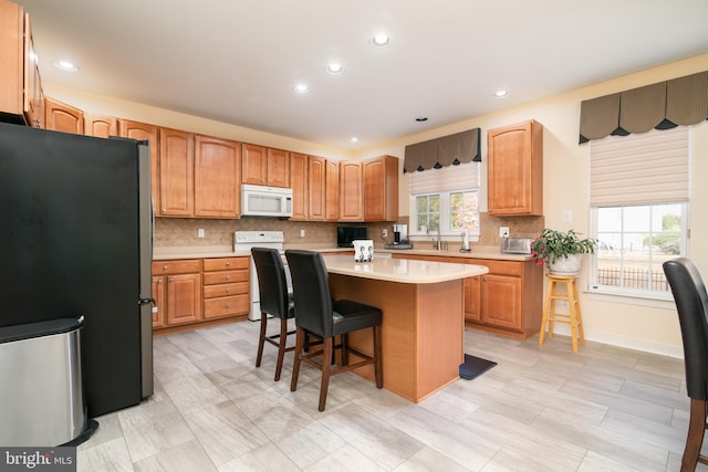 kitchen with white appliances, a breakfast bar area, a wealth of natural light, and a center island