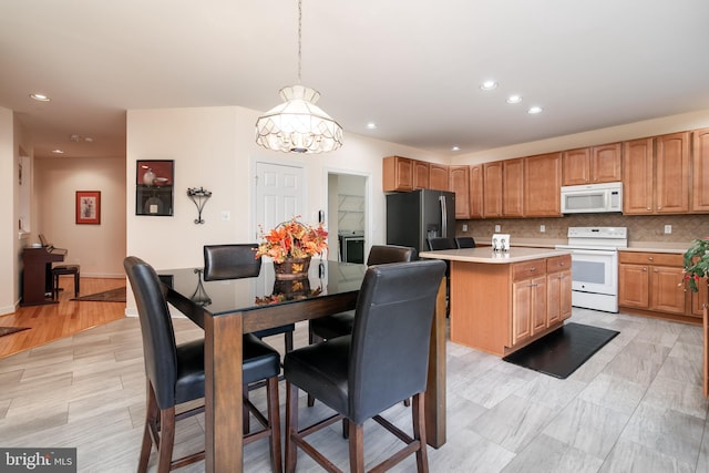 kitchen featuring an inviting chandelier, white appliances, a center island, pendant lighting, and decorative backsplash