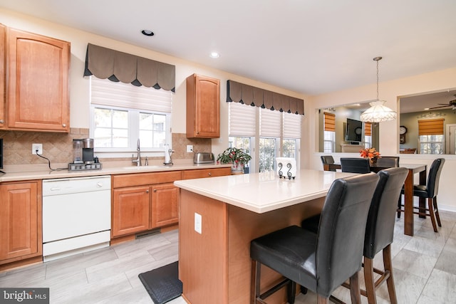 kitchen featuring tasteful backsplash, white dishwasher, hanging light fixtures, sink, and a center island