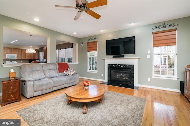 living room featuring light wood-type flooring, a high end fireplace, ceiling fan, and plenty of natural light