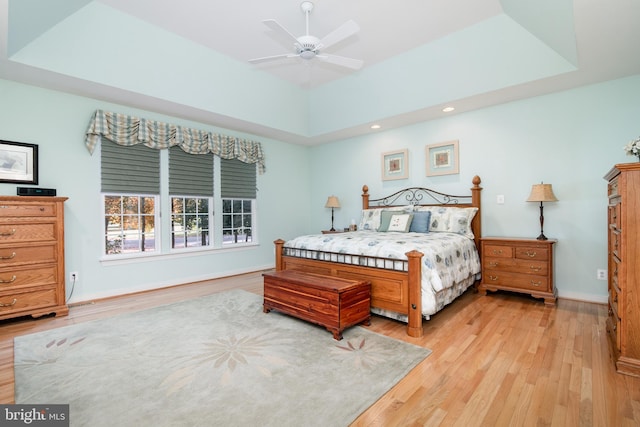 bedroom featuring light hardwood / wood-style floors, ceiling fan, and a raised ceiling