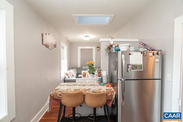 kitchen with dark hardwood / wood-style flooring, a breakfast bar, a skylight, and stainless steel refrigerator