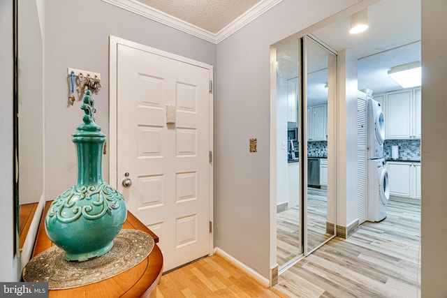 foyer entrance featuring light wood-type flooring, ornamental molding, a textured ceiling, and stacked washer and clothes dryer