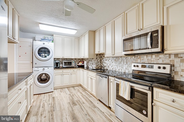 kitchen featuring decorative backsplash, appliances with stainless steel finishes, dark stone countertops, light hardwood / wood-style floors, and stacked washer and clothes dryer