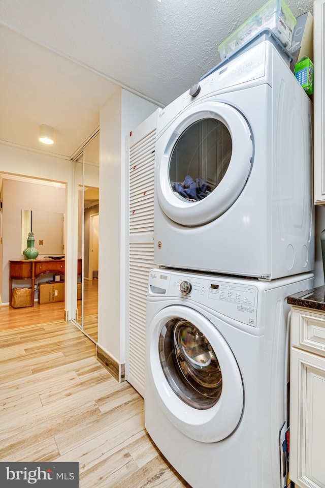 washroom with a textured ceiling, stacked washer and dryer, and light wood-type flooring