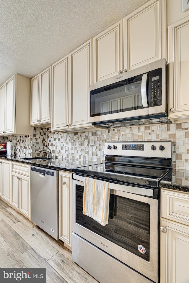 kitchen featuring stainless steel appliances, cream cabinets, and light wood-type flooring