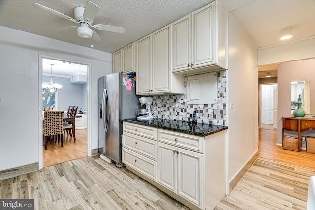 kitchen with dark stone countertops, crown molding, light wood-type flooring, ceiling fan with notable chandelier, and tasteful backsplash