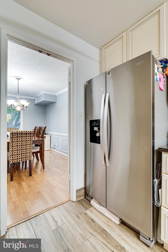 kitchen featuring stainless steel fridge, an inviting chandelier, ornamental molding, light hardwood / wood-style floors, and decorative light fixtures