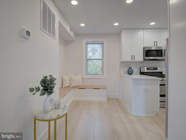 kitchen featuring appliances with stainless steel finishes, decorative backsplash, light hardwood / wood-style floors, and white cabinets