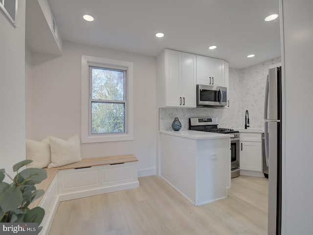 kitchen with stainless steel appliances, white cabinets, and light wood-type flooring