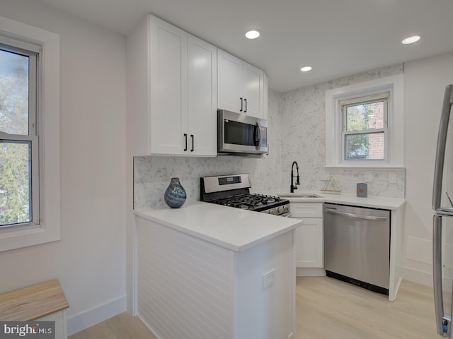 kitchen featuring white cabinetry, appliances with stainless steel finishes, sink, decorative backsplash, and light hardwood / wood-style flooring