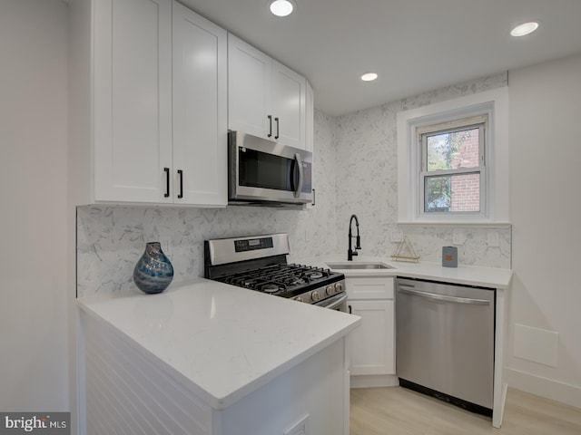 kitchen with white cabinetry, appliances with stainless steel finishes, backsplash, sink, and light hardwood / wood-style flooring