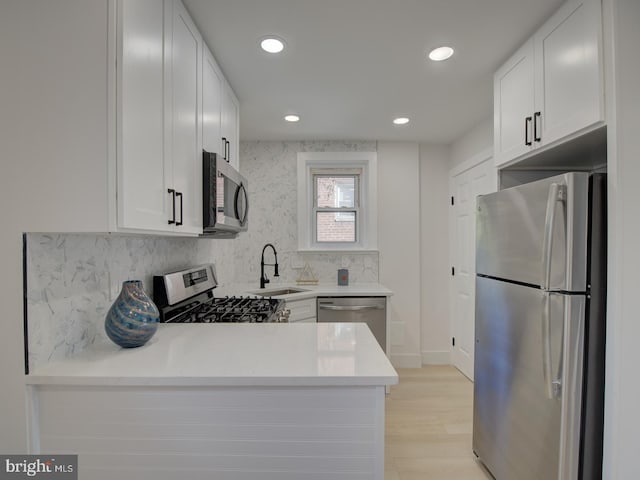 kitchen with white cabinetry, sink, kitchen peninsula, appliances with stainless steel finishes, and light hardwood / wood-style flooring