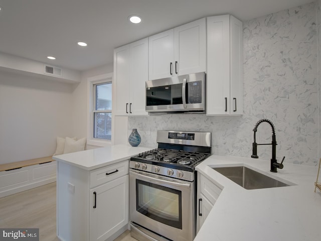 kitchen with white cabinetry, appliances with stainless steel finishes, light wood-type flooring, sink, and kitchen peninsula