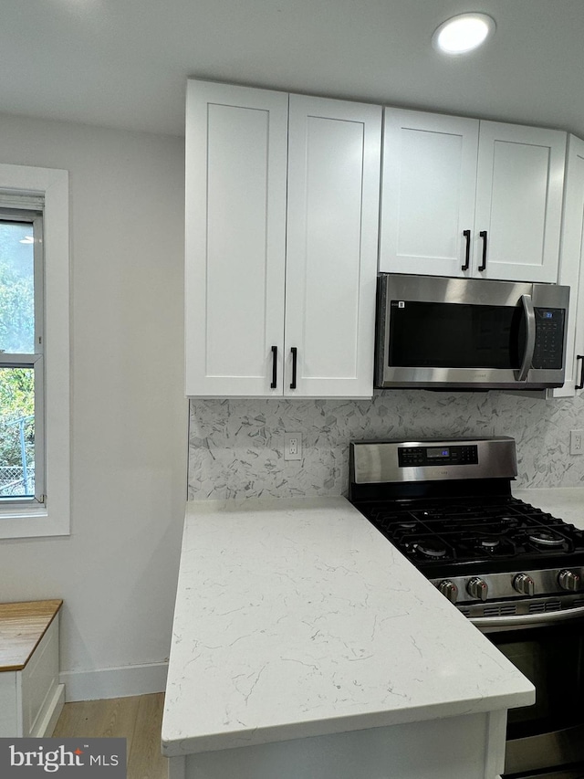 kitchen with stainless steel appliances, light hardwood / wood-style floors, white cabinets, and backsplash