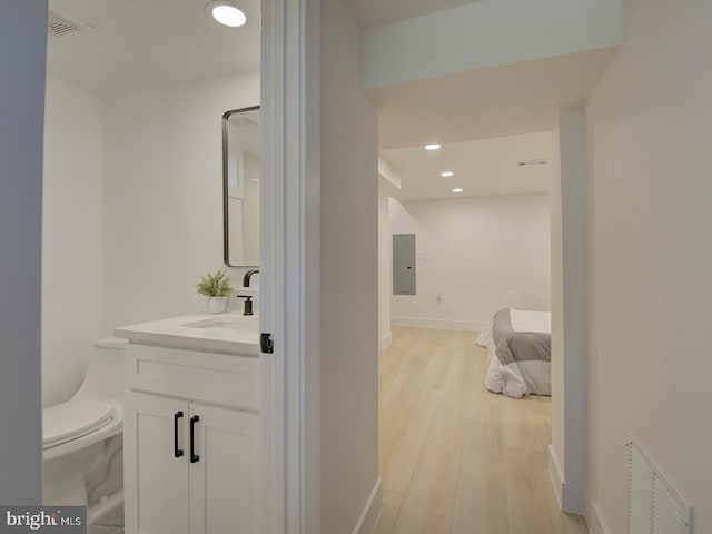 bathroom with electric panel, wood-type flooring, toilet, and vanity