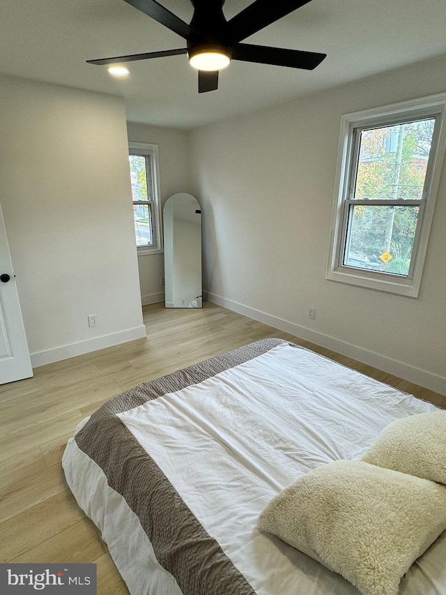 bedroom featuring ceiling fan, multiple windows, and light hardwood / wood-style flooring