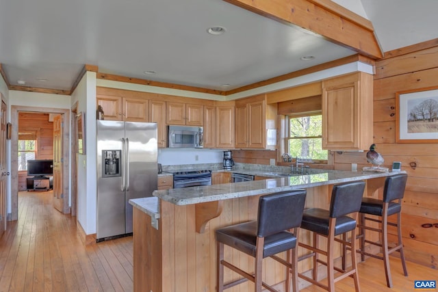 kitchen with wood walls, light stone countertops, appliances with stainless steel finishes, light wood-type flooring, and a breakfast bar