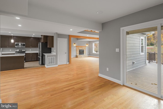 kitchen with a stone fireplace, dark brown cabinets, a healthy amount of sunlight, and appliances with stainless steel finishes