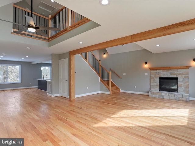 unfurnished living room with light wood-type flooring, baseboards, a stone fireplace, and recessed lighting