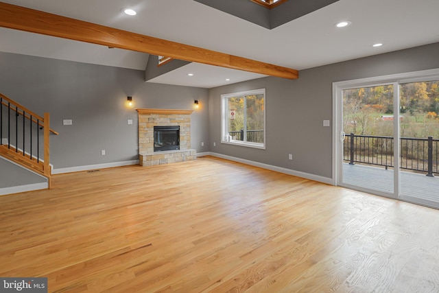 unfurnished living room featuring lofted ceiling with beams, plenty of natural light, a stone fireplace, and light hardwood / wood-style floors