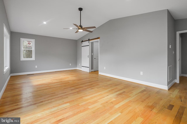 spare room featuring ceiling fan, lofted ceiling, a barn door, and light hardwood / wood-style floors