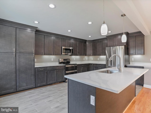 kitchen with a sink, stainless steel appliances, pendant lighting, light wood finished floors, and dark brown cabinets