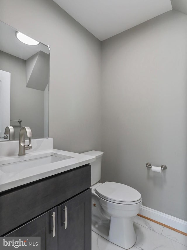 half bath featuring toilet, marble finish floor, baseboards, and vanity