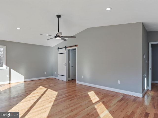 empty room featuring lofted ceiling, a barn door, baseboards, ceiling fan, and light wood-type flooring