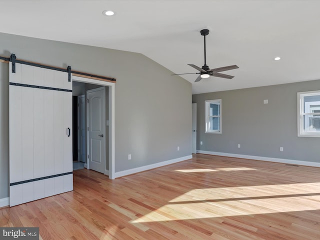 unfurnished bedroom with baseboards, a barn door, light wood-style floors, lofted ceiling, and recessed lighting