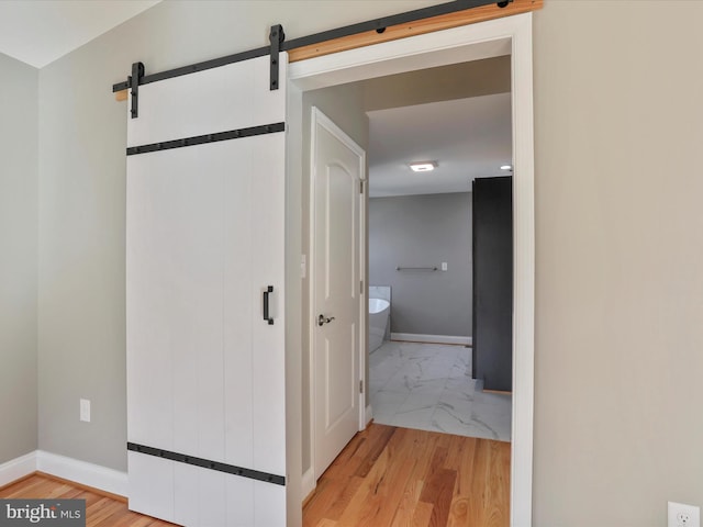 corridor with marble finish floor, a barn door, and baseboards